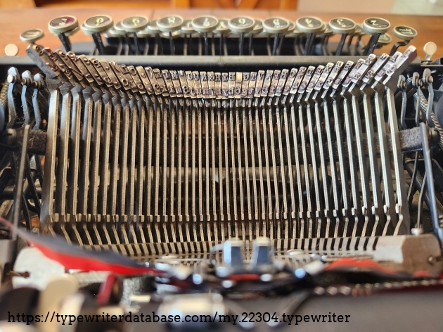 Reverse view into the opened Smith-Corona Clipper featuring a close up view of all of the type face and levers. Just visible at the top are a side view of the keys on the front of the typewriter.