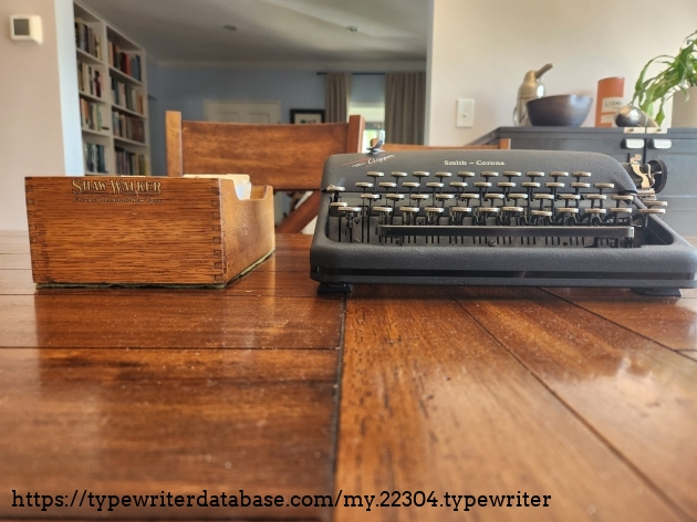 Desk level view of the front of a Shaw-Walker wooden card index tray next to a black typewriter.