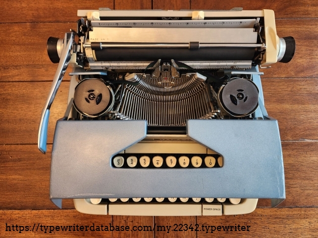 The typewriter with it's hood slid forward to see the type-bars and ribbon inside.