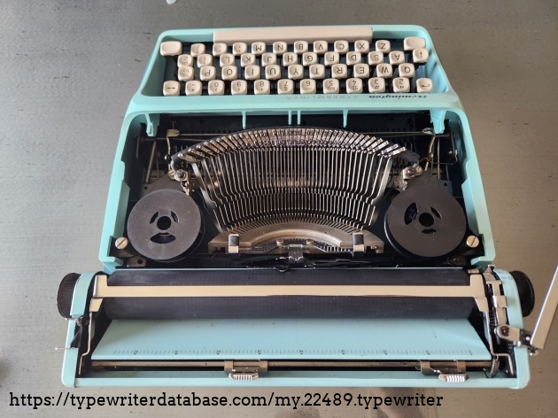 Overhead view from behind of Remington Streamliner typewriter with the hood removed to allow a view into the typebasket featuring all the typebars and pica typeface as well as two plastic ribbon spools.