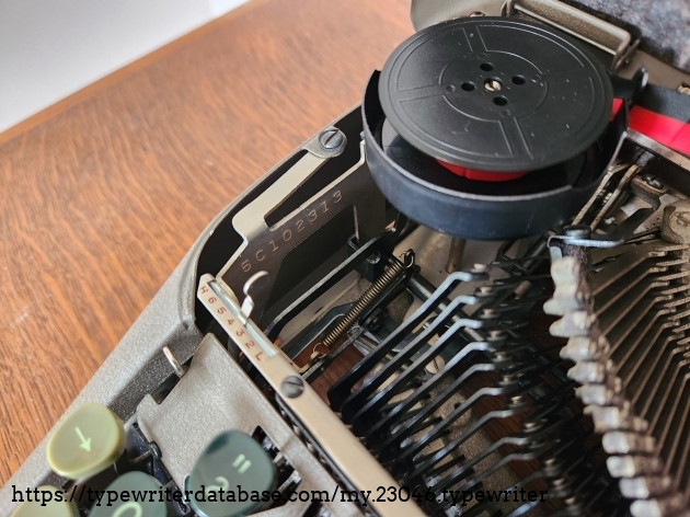 View of the inside left of the typewriter with the hood up showing the left ribbon cup, the touch controls and visibly stamped into a metal bar between them is the serial number of the machine