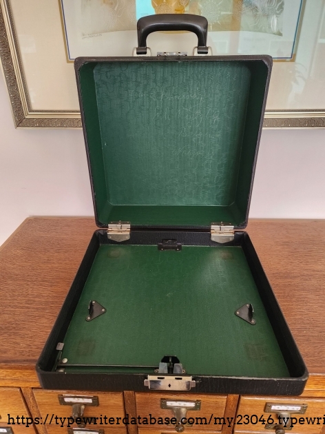 Opened black Smith-Corona case with green interior sitting on a wooden library card catalog.