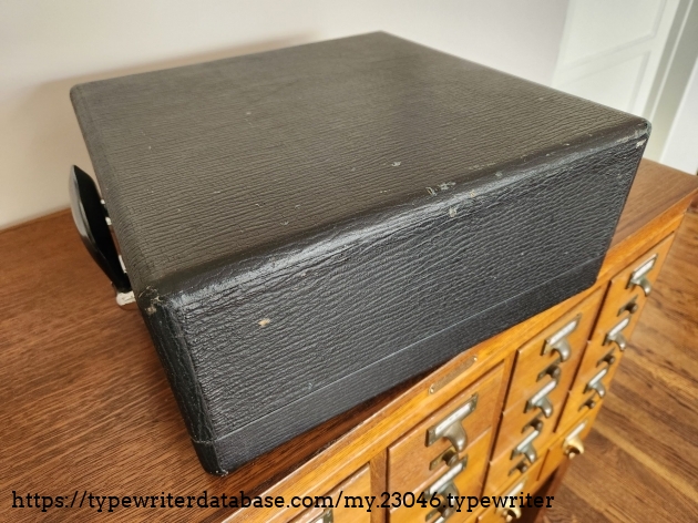 Angle on three sides of the black fabric covered typewriter case sitting on a library card catalog.