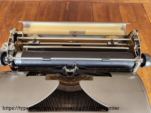 Focus on the carriage and opened paper table of a Remington All-New typewriter. With the paper table open one can see the two margin stops. Uncommon are several strips of cream colored masking tape covering the inside of the metal paper table cover.