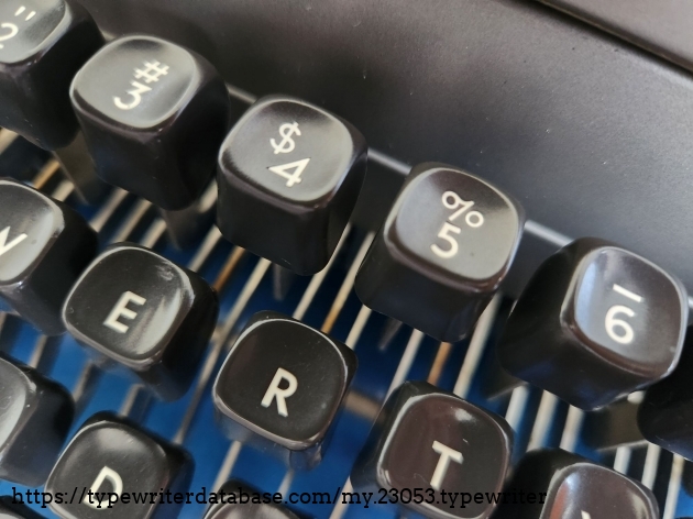 Close up of the dark gray typewriter keys on the top two rows. Of interest are the $ and 4 which aren't directly over each other as on most number keys, but they're staggered at an angle.