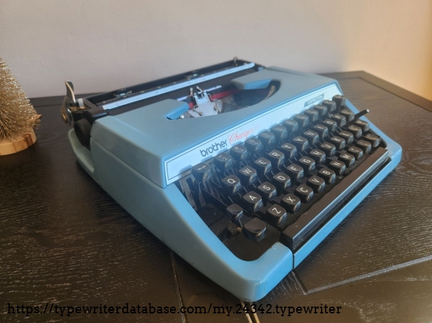 Oblique angle from the left side featuring a Brother Charger 11, a small blue metal portable typewriter with black keys.