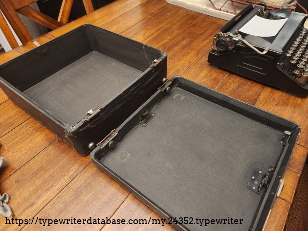 Black wooden typewriter case covered in black material. It's split into two parts and sitting on a wooden table in front of a 1941 Corona Standard "Flat top" in the background.