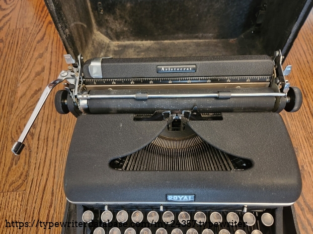 Focusing on the hood and carriage of a 1939 Royal Aristocrat typewriter from above. A bit dusty and dirty with flecks of correction ribbon around the typing point.