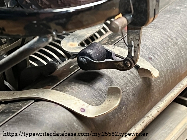 Black ink on this roller. [Update: It's actually purple.] The amount of pressure applied on the paper by these two paper arms/fingers can be adjusted by knurled thumb screws on either side of the typewriter.