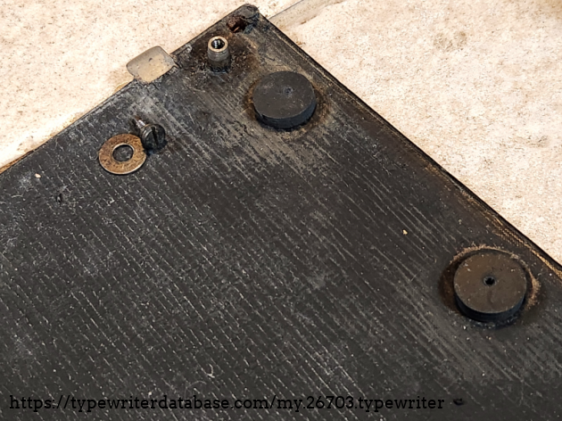 Showing the pads below the between the body and the case bottom as well as the screw and washer used to bolt the body to it. Normally, these typewriters would be used still attached to the case bottom. That is why this is retained here but the case top is missing. Showing the pads below the between the body and the case bottom as well as the screw and washer used to bolt the body to it. Normally, these typewriters would be used still attached to the case bottom. That is why this is retained here but the case top is missing.