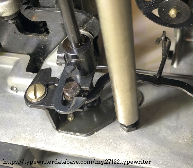 The mechanism for choosing the ribbon colour.
The wire hook on the right determines the bold to go up (black), be in the middle (void) or down (red).  
The flat steel push lever on the right actuates the hopper at any keystroke. 
The bolt  jammed itself in the slot  bcause the flat steel push lever on the right was bend. It bends under load, so if it jams, it jams more.