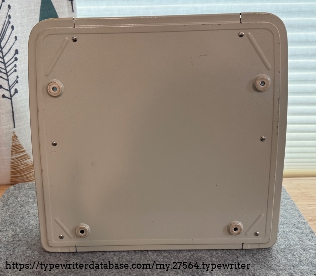 Bottom of the typewriter. The rubber grommets are a bit worn but still in good shape. They are cream like the case.