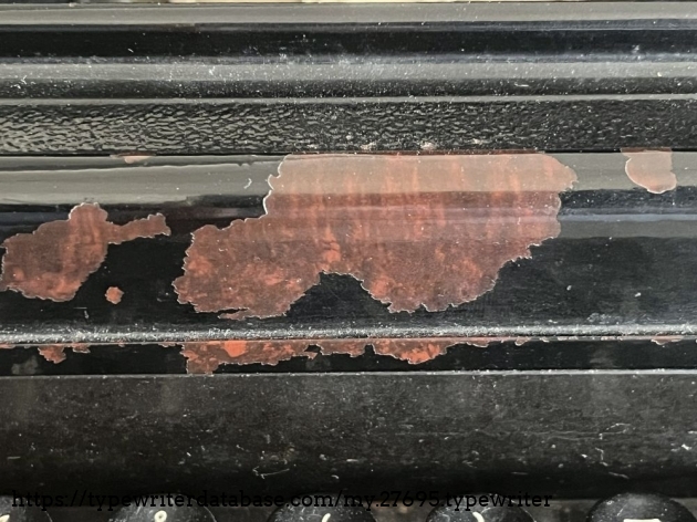 Detail: overcoating; these damages show that the Bakelite ribbon cover which previously had an Art Deco-style, reddish-brown marbling, was subsequently painted over in black.