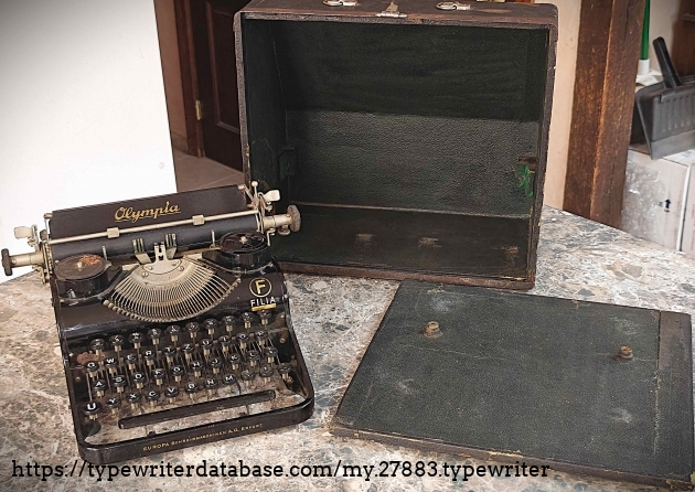 Typewriter with case.  The machine is supposed to bolt to the case.  Unfortunately, both mounting screws are missing, and one of the threaded rod inserts is also missing.  It seems a key (also missing) is needed to latch the case.