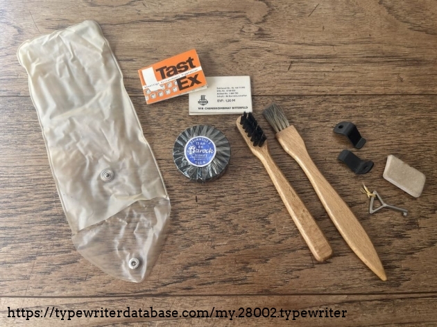 Detail: cleaning supplies, the case key, a rubber gum, a still unfoiled ribbon spool, two booklets of "Tast Ex", the socialist equivalent to Tipp Ex. And, at last, two metal parts whose purpose I don't know (possibly for mounting the typewriter to the case bottom?)