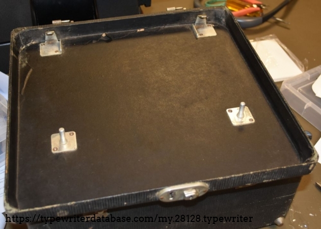 The Underwood portables of this era used this system to affix the typewriter to the case.  The rear claws hook over the rear feet area, and the posts fit into the holes in the front feet.  It relies on friction to stay, but once the lid is closed, the typewriter is not able to come off the posts.