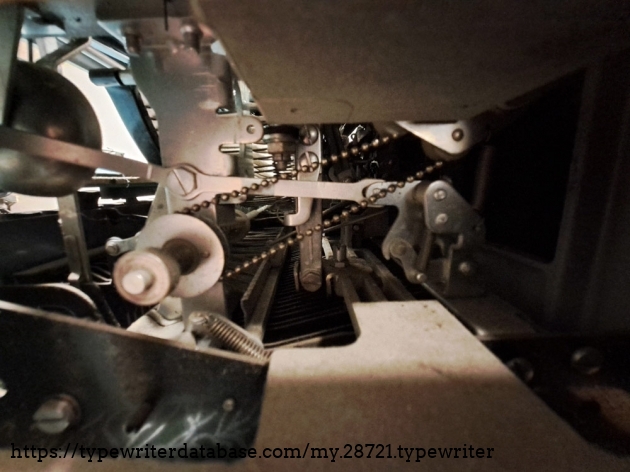 View through the side access port, showing the ball-chain drive for the ribbon.  Oddly, this machine advance the ribbon even when the spacebar is pressed.