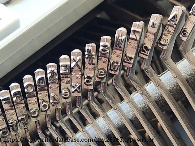 Close up of the slugs on the left hand side of a 1971 Hermes 3000 featuring a san serif Epoca typeface. The foundry mark on the slugs is "S NO".