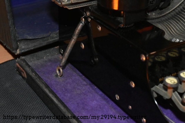 Detail of the case attachment mechanism, which is a spring that is hooked onto the body of the typewriter.