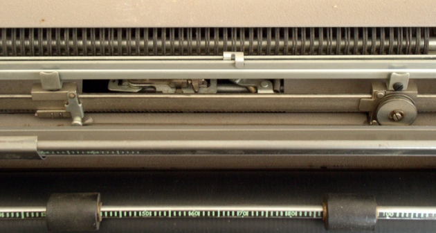 This is the "automatic Margin" system; it's a miniature of the carriage return spring & drawband and it's located under the paper table.