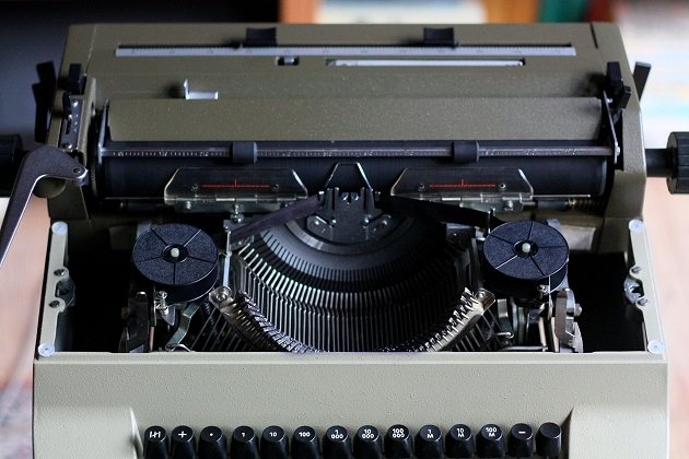 Removing the ribbon cover shows this typewriter to be a straight descendant of the Optima M10, M14, etc: there's lots of stowing space on the sides of the mechanism